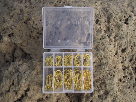 on large stone is an open box made of translucent plastic with fishing hooks of different numbers in gold color.の写真素材
