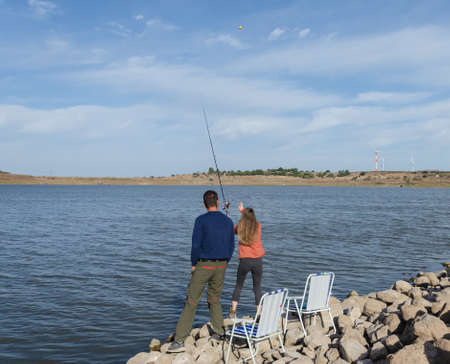 girl throws a fishing rod into the lake, guy stands nearby and looks at herの写真素材
