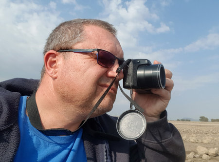 a man in sunglasses holds a camera with one hand and photographs the landscape of a rocky plainの写真素材