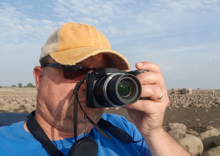 a man in sunglasses holds a camera with one hand and photographs the landscape of a rocky plainの写真素材