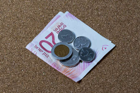 on a paper bill of twenty shekels folded in half there is a pile of coins of different denominationsの写真素材