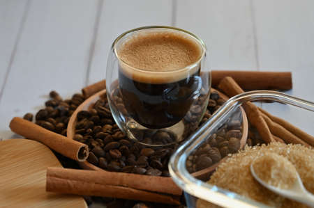 a glass glass stands on coffee beans in a wooden plate next to a sugar bowl with brown sugar close upの写真素材
