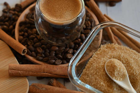 a glass glass stands on coffee beans in a wooden plate next to a sugar bowl with brown sugar close upの写真素材