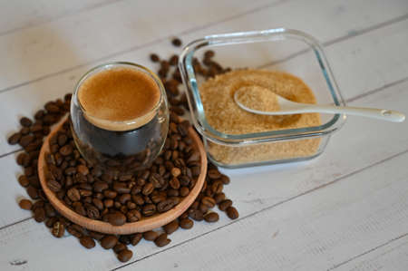 a glass glass stands on coffee beans in a wooden plate next to a sugar bowl with brown sugar close upの写真素材