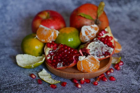 A pomegranate, whole and broken into pieces with other fruits, lies on a marble table close-upの写真素材