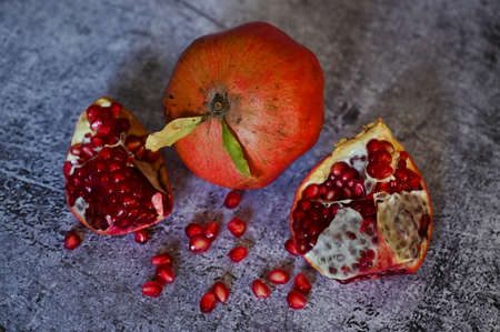 The pomegranate, whole and broken into pieces, lies on a wooden plate on the tableclothの写真素材