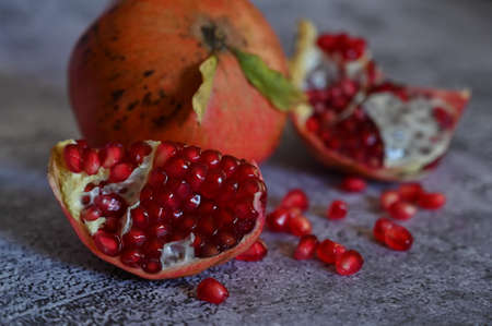 The pomegranate, whole and broken into pieces, lies on a wooden plate on the tableclothの写真素材