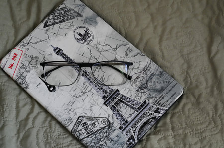 the tablet in the case is lying on the bed with glasses on it carelessly