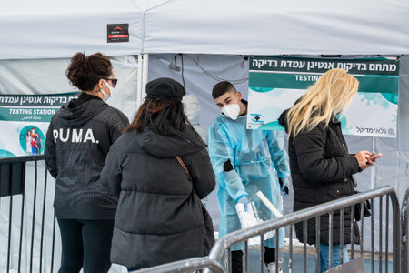 Netanya, Israel, February 7, 2022: Herzel street.A paramedic in personal protective equipment PPE receives people for vaccination. COVID-19 pandemic outbreak crisis, worried exhausted staff.のeditorial素材