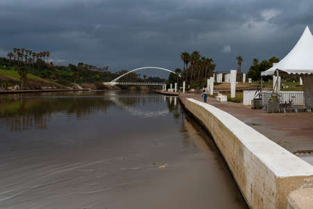 An arc bridge over the river in a recreation and amusement park. In the water you can see the reflection of the bridge on the right, a walking area. overcast sky.の写真素材