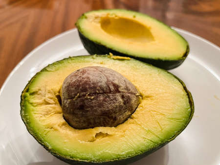 Healthy green avocado cut in half on a white plate with pit. close-up.