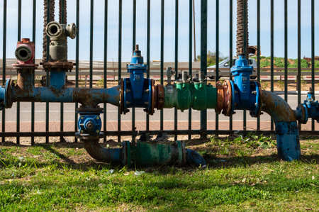 Industrial water pipes with valves and hose connections are located above the ground in the park. close-up.の写真素材