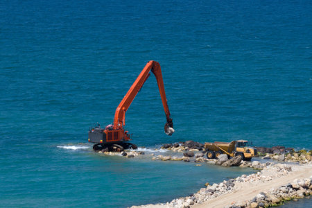 An excavator and a mining truck move stones into the sea. Construction of breakwaters to protect the...