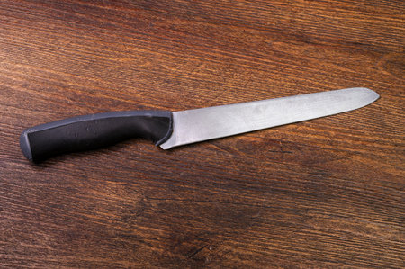 a kitchen knife with a black handle lies on a dark wooden background. High quality photo