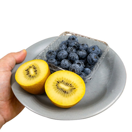 Fresh blueberries and kiwi halves on a plate in hand on a white background. High quality photoの写真素材