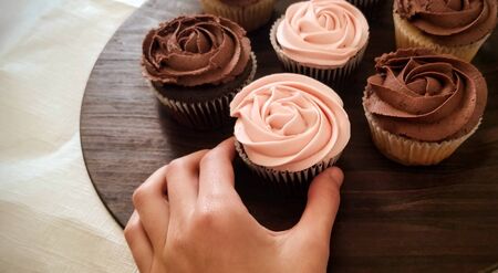 wooden tray of pink and brown iced cupcakes being grabbed by child's hand