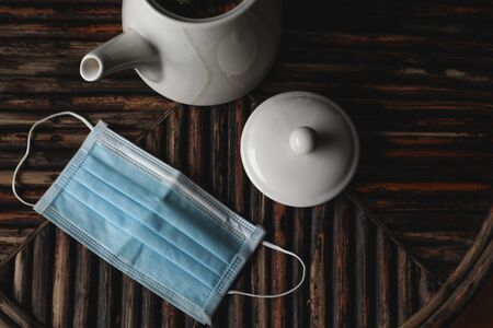 face mask and pot of tea put on dark wooden table