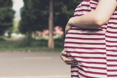 Beautiful pregnant woman in a sunset outside in the park, touching belly