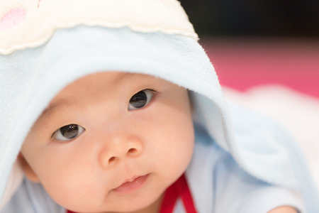 A little boy baby is hiding under a blue blanket. He is staring at the camera and posing on his tummy. Use it for a childhood, parenting or love concept.の写真素材