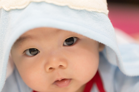 A little boy baby is hiding under a blue blanket. He is staring at the camera and posing on his tummy. Use it for a childhood, parenting or love concept.の写真素材