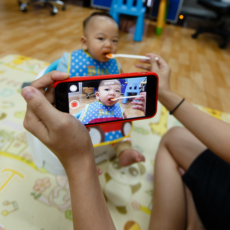 Asian mother take a video of her baby boy eating with smartphone focused on the deviceの写真素材