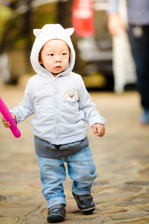 Full-length portrait of adorable little boy wearing jacket with hood. Hands hold twisting balloon.の写真素材