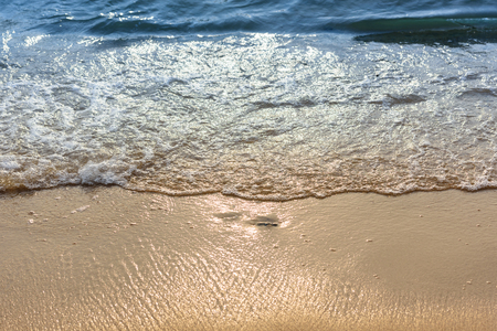 Soft wave of the sea on the sand beach with sunlight. Tropical sandy beach background with copy space. Top down view.の写真素材