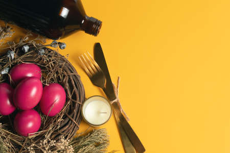 easter eggs pink on yellow background with spoon and fork and dried grass with wood vine and flower...