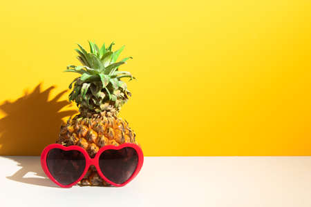 pineapple tropical fruit with fashion red heart sunglasses, hot summer season vacation holiday, yellow background, sunshine day, paradise travel tour and relax conceptの写真素材
