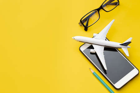 airplane with eyeglasses and smartphone with pencil on yellow background in travel tour booking conceptの写真素材