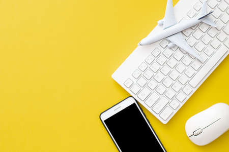 airplane with smartphone with mouse and keyboard on yellow background in travel around the world tour booking conceptの写真素材