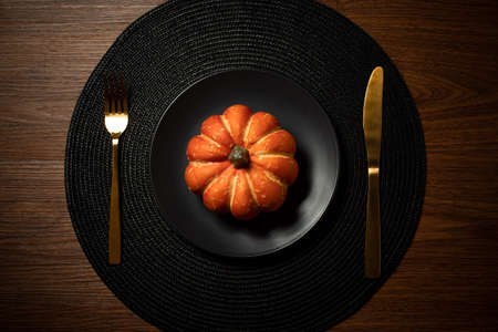 gold spoon food and black dinner dish with halloween pumpkin on wood table background top view