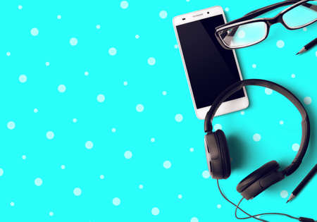 smartphone with pencila and headphone with eyeglasses on blue green table background in business at home connceptの写真素材
