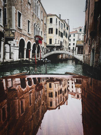 Houses reflections on the Varnished wooden hood, pontoon, of the water taxi in the streets of Venice, which leavesの写真素材