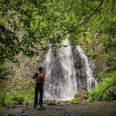 Back view on a man hiker looking Queureuilh waterfall, Le Mont-Dore, Puy-de-Dome, Auvergne, Franceの写真素材