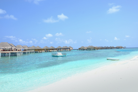 A boat rests peacefully on the clear blue shallow waters beside the bungalows. Maldive Islands.の写真素材