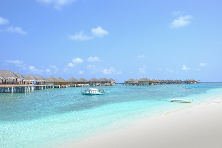 A boat rests peacefully on the clear blue shallow waters beside the bungalows. Maldive Islands.のeditorial素材