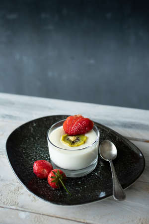 Yogurt with fresh strawberries and kiwi on a black plateの写真素材