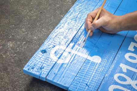A man writing signs board with a brush of watercolors on cement floor background. Painting on wooden board in thai language for advertising.の写真素材