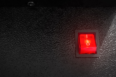 Red power switch on dark background. Electric control button.