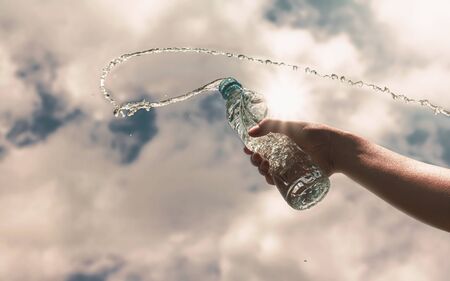 Hand holding a clear plastic bottle of pure drinking water refreshing and splash on a hot background with a hungry and thirsty concept for good health.の写真素材