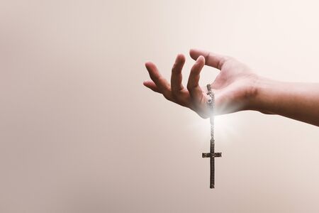 Praying hands hold a crucifix or cross of metal necklace with faith in religion and belief in God on...