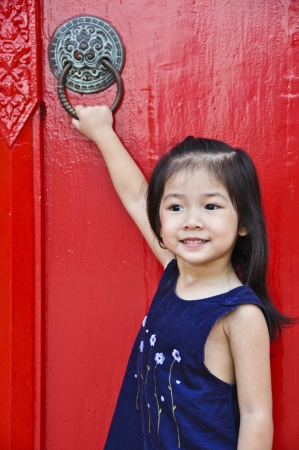 Little asian pretty girl in front of ancient red door の写真素材