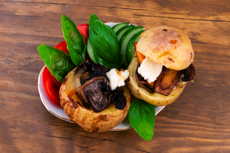 Baked potato tubers in the oven, stuffed with fried mushrooms with onions and carrots, decorated with slices of tomatoes, cucumbers and basil leaves.の写真素材