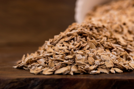 Oat flakes scattered on a table of an overturned white plate, close-up on a wooden background.の写真素材