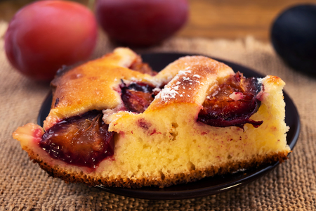 A portion of the pie with plums on a round plate on the background of ripe plums purple and blue, close-up.の写真素材