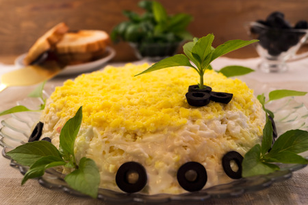 Salad on a glass plate with a top layer of egg yolks, decorated with chopped black olives and green basil leaves.の写真素材