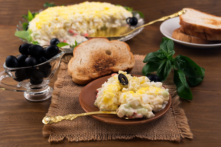 Appetizer for the holiday table of crab meat, cheese, eggs and cucumber, near basil  leaves, pickled olives, toasted toast.の写真素材