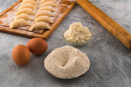 Sifted flour on a round plate, cottage cheese for filling,  eggs  ingredients for cooking homemade dumplings.の写真素材