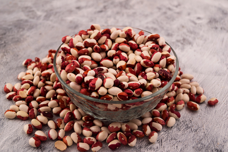 Round glass bowl with two-color beans, scattered beans on wooden background.